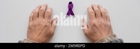 top view of cropped male hands near purple alzheimer disease awareness ribbon on white surface, banner,stock image Stock Photo
