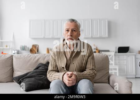 senior grey haired man with azheimers syndrome sitting on couch at home and looking at camera,stock image Stock Photo