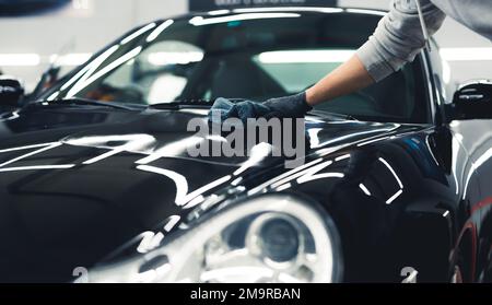 Man using a microfiber cloth to apply ceramic coating onto a shiny expensive black car. Unrecognizable person in protective gloves. High quality photo Stock Photo