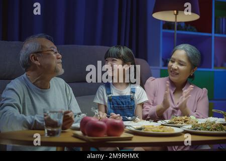 family grandmother grandfather and granddaughter dining on table and having fun during Stock Photo