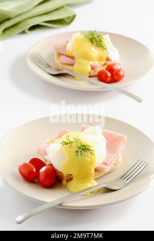 Two Eggs Benedict with cherry tomatoes on cream plates with white background in vertical format.  Healthy, nutritious breakfast or lunch. Stock Photo