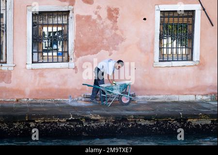 A construction worker works on patching the colorful side of a building in Venice on the Grand Canal. Stock Photo