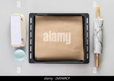 Baking tray with parchment paper, rolling pin, egg holder and paper forms on light background Stock Photo