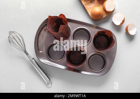 Muffin baking tray with paper forms, whisk and eggs on light background Stock Photo