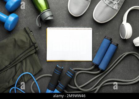 Blank notebook with sports equipment, bottle, headphones and sneakers on dark background Stock Photo