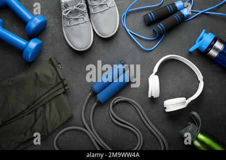 Skipping ropes with dumbbells, bottles, headphones, sneakers and clothes on dark background Stock Photo