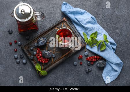 Board with glass cup of fruit tea, berries, teapot and napkin on dark background Stock Photo