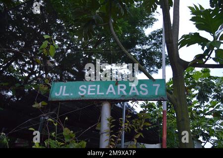 Portrait of a street sign with bright green that reads 'JL. SELARAS 7', with trees in the background. Stock Photo