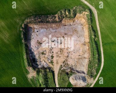 View from a high altitude of a stone quarry dug in the middle of a green field, limestone open pit mining Stock Photo