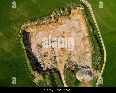 View from a high altitude of a stone quarry dug in the middle of a green field, limestone open pit mining Stock Photo