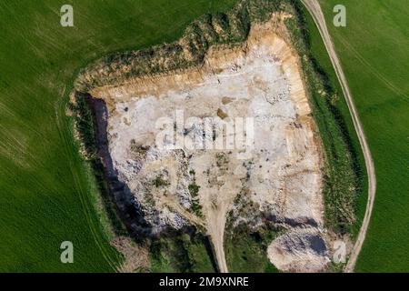 View from a high altitude of a stone quarry dug in the middle of a green field, limestone open pit mining Stock Photo