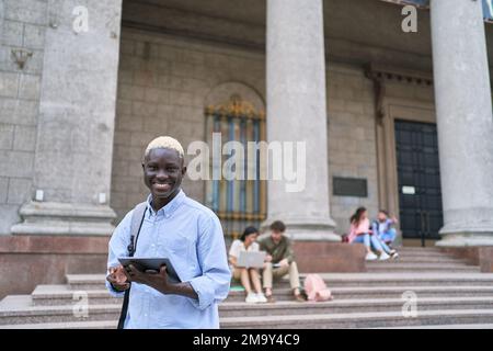 student looking at the screen with a digital tablet standing in front of the university. Stock Photo