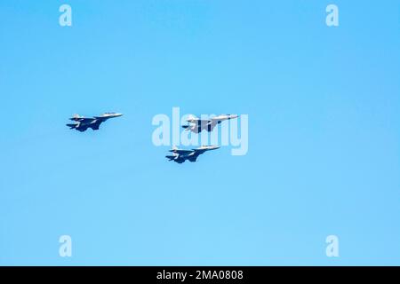 Flying aircraft with Vic formation against isolated blue sky. Three supersonic fighter plane forming Arrowhead. Stock Photo