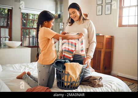 Laundry, pregnant mother and child help with house chores and cleaning with love and care. Folding clothes, happy and working family in a bedroom bed Stock Photo