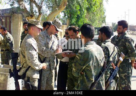 040605-M-4419R-020. [Complete] Scene Caption: US Marine Corps (USMC) Sergeant (SGT) Jason L. Booth, Charlie Company (C CO), 1ST Battalion (BN), 5th Marines (1/5), Regimental Combat Team 1 (RCT 1), 1ST Marine Division (MAR DIV), has Iraqi Civil Defense Corps (ICDC) Soldiers sign the pay roster to be paid, as other USMC Marines watch. The training of the ICDC Soldiers is taking place at India Base in Nasir Waal Salaam, Iraq (IRQ). Some of the Iraqi Soldiers are wearing their new desert uniforms. The 1ST MAR DIV, in support of Operation IRAQI FREEDOM, is engaged in Security and Stabilization Oper Stock Photo