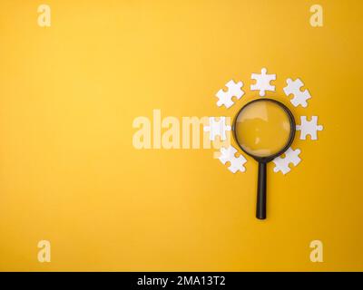 Magnifying glass searching missing puzzle on yellow background Stock Photo