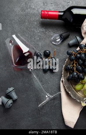 An overhead photo of glasses of red wine with a bottle, grapes, and a vintage corkscew and corks, shot from above on a dark background. Top view. Stock Photo