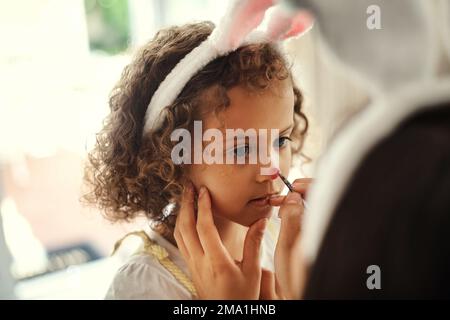 Do you want a red nose. a woman painting her daughters face during the easter holiday. Stock Photo