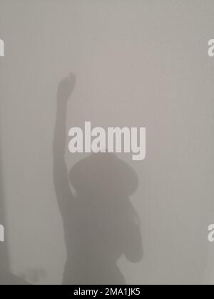 Shadow silhouette of woman in a hat with raised hand on a white wall Stock Photo