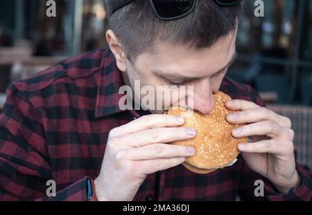 Portrait of hungry man eating burger in city cafe. Stock Photo