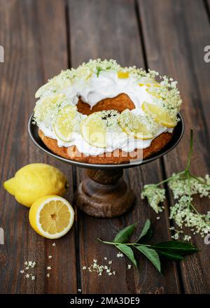 Homemade ring cake, over a doily with sugar icing, lemon slices and elder blossoms on a rustic table. Copy space. Stock Photo