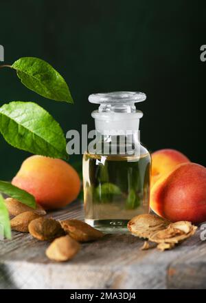 Apothecary glass of apricot kernel oil with apricot kernels and ripe apricots on a rustic wooden table. Fruit aroma oil. Natural cosmetics.