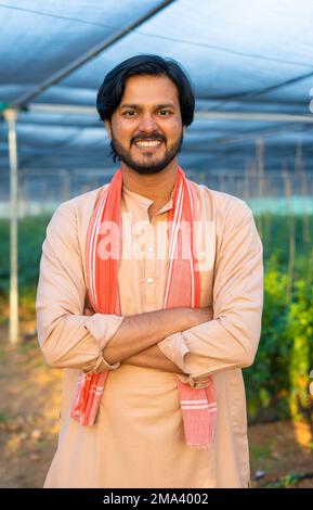 vertical portrait shot of happy young farmer confidently smiling by looking at greenhouse - concept of entrepreneur, modern farming and small agri Stock Photo