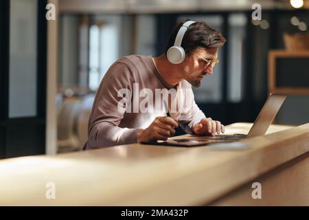 Graphic designer busy with a project in a cafe. Male design professional working with a laptop and a graphics tablet. Creative business man working re Stock Photo
