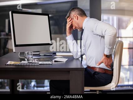 That terrible pain is back. a businessman experiencing back pain while sitting at his desk. Stock Photo