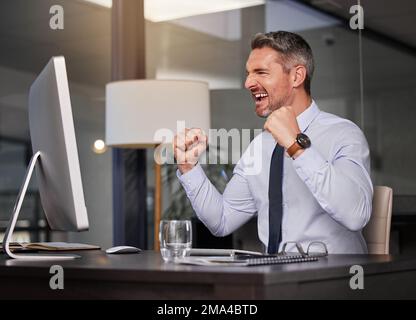 Its important to celebrate your victories, even the small ones. a businessman looking cheerful while sitting at his desk. Stock Photo