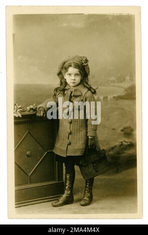 Gorgeous original Edwardian era studio portrait postcard of very cute Edwardian young girl with long curly hair and wearing a knitted coat and beret, holding a leather briefcase, schoolgirl, circa 1910, U.K. Stock Photo
