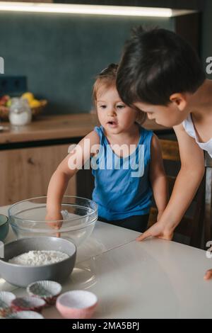 Loving young kids preparing pancakes or biscuits, make breakfast at home together. Happy family. People lifestyle. Food preparation. Sweet food. Stock Photo