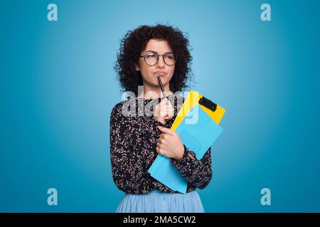 Young curly-haired student woman isolated on blue background having doubts. Stock Photo