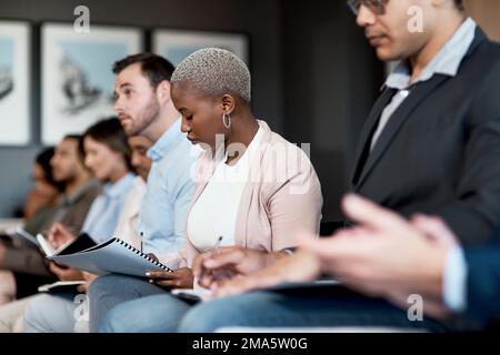 Sit down and listen. a group of businesspeople making notes during a conference in a modern office. Stock Photo