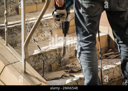 Man removes tiles from a stair using a hammer drill Stock Photo
