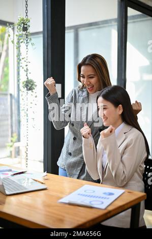 Portrait, Two cheerful and excited millennial Asian businesswomen celebrating their project success together in the office. Stock Photo