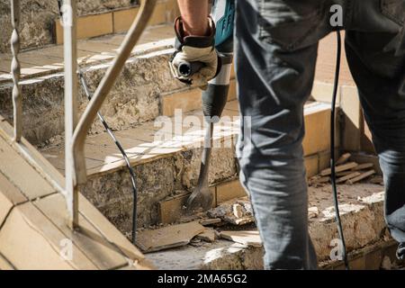 Man removes tiles from a stair using a hammer drill Stock Photo