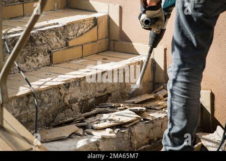 Man removes tiles from a stair using a hammer drill Stock Photo