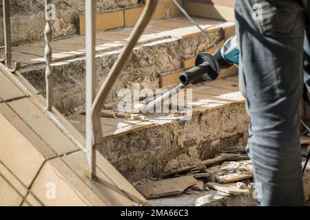 Man removes tiles from a stair using a hammer drill Stock Photo