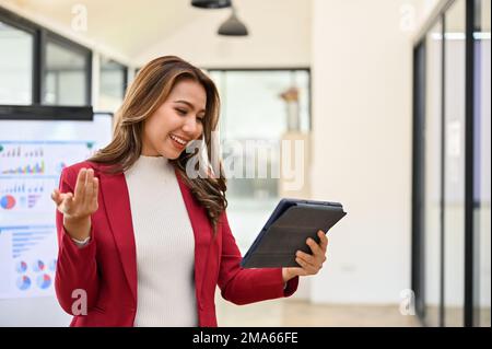 Cheerful and happy millennial Asian businesswoman or female CEO looking at her tablet screen, surprised with business's result on tablet screen while Stock Photo