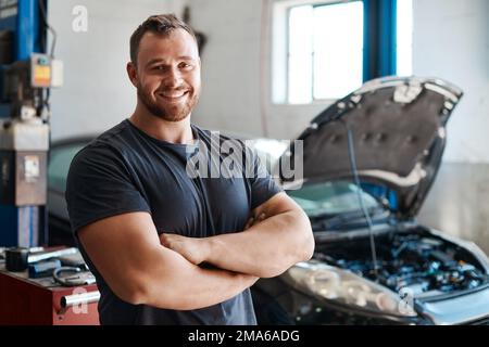 Looking for a trustworthy mechanic Hes your guy. a mechanic posing with his arms crossed in an auto repair shop. Stock Photo