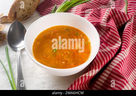 White plate with red borsch on the table. Traditional Ukrainian vegetable soup made from beets, carrots, tomatoes, potatoes, cabbage, greens and garli Stock Photo