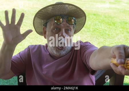 Outdoor portrait of bearded Caucasian senior making selfie with pure emotions on his face while resting in summer garden Stock Photo