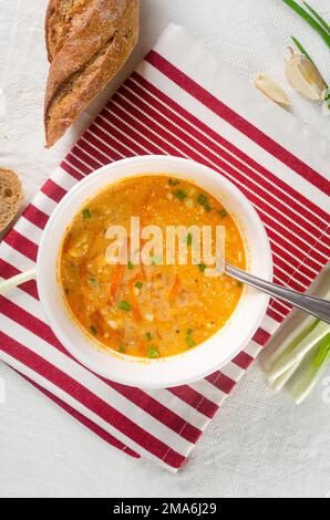 White plate with red borsch on the table. Traditional Ukrainian vegetable soup made from beets, carrots, tomatoes, potatoes, cabbage, greens and garli Stock Photo