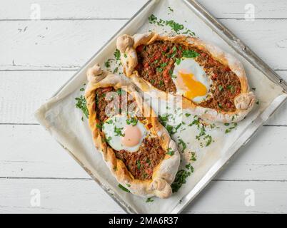 Turkish Pide with spicy minced meat filling and poached egg topping on a background isolated on white background. Flat lay Stock Photo