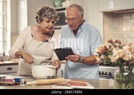What ingredients do we need. a senior couple using a digital tablet while baking at home. Stock Photo