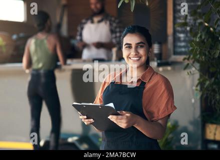 Table for. an attractive young woman standing outside her restaurant and holding a clipboard. Stock Photo