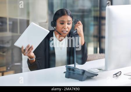 I dont know what to do anymore. an attractive young businesswoman sitting alone and feeling stressed while wearing a headset and using a telephone. Stock Photo