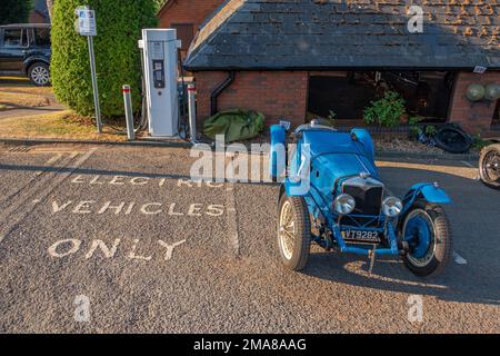 Blue 1933 Riley TT Sprite Classic car parked next to a Electric vehicles only charging point in low morning sun. Stock Photo