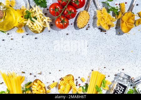 Various dried  spaghetti, noodles, pasta  set in spoons on white table background. Different shapes types raw italian pasta with herbs, olive oil, tom Stock Photo